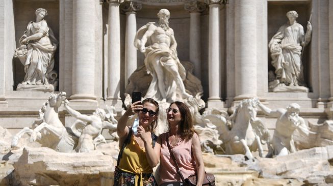 Warga berswafoto tanpa mengenakan masker pelindung di depan Air Mancur Trevi, Roma, pada (28/6/2021). [Filippo MONTEFORTE / AFP]