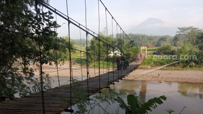 Warga menyebrangi “jembatan seribu janji” yang menghubungkan Kecamatan Bandongan, Kabupaten Magelang dan Kecamatan Kramat Utara, Kota Magelang. (suara.com/ Angga Haksoro Ardhi).