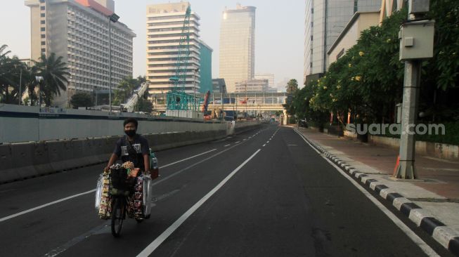 Pedagang melintas di Jalan M.H Thamrin, Jakarta, Sabtu (3/7). [Suara.com/Oke Atmaja]
