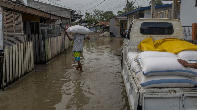 Warga memikul beras ke rumahnya yang digenangi air akibat sungai meluap di Kelurahan Baru, Palu, Sulawesi Tengah, Sabtu (3/7/2021). [ANTARA FOTO/Basri Marzuki]