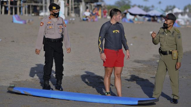 Petugas Satpol PP dan Polisi meminta wisatawan untuk meninggalkan objek wisata pantai yang ditutup saat melakukan pengawasan Pemberlakuan Pembatasan Kegiatan Masyarakat (PPKM) Darurat di kawasan Canggu, Badung, Bali, Minggu (4/7/2021). [ANTARA FOTO/Fikri Yusuf]