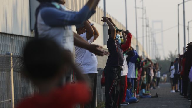 Warga mengikuti senam bersama di hari kedua PPKM Darurat di Jembatan Suramadu, Surabaya, Jawa Timur, Minggu (4/7/2021). [ANTARA FOTO/Didik Suhartono]