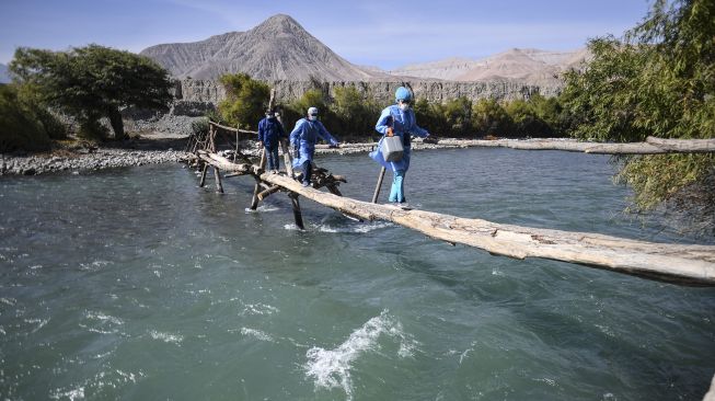 Petugas kesehatan menyeberangi Sungai Camana untuk menyuntik warga lanjut usia dengan dosis vaksin Pfizer-BioNTech melawan COVID-19 di Arequipa, Peru, pada (2/7/2021). [Diego Ramos / AFP]