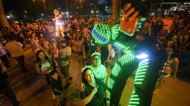 Orang-orang berfoto dengan penghibur berkostum RoboTron di atas panggung selama Festival UFO di Roswell, New Mexico, pada (2/7/2021). [Patrick T. FALLON / AFP]