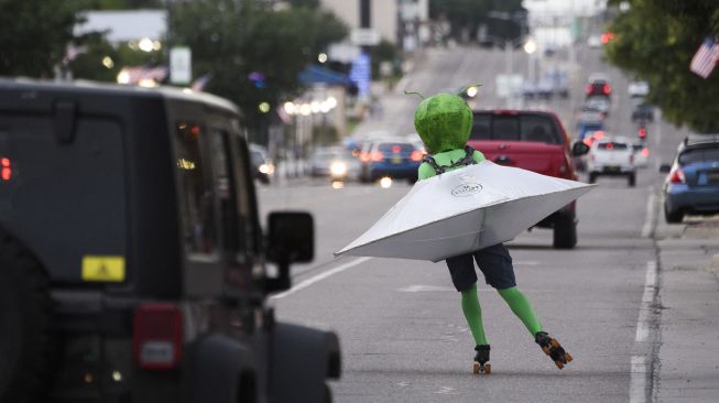 Seseorang mengenakan kostum alien dalam sepatu roda piring terbang melintas selama Festival UFO di Roswell, New Mexico, pada (2/7/2021). [Patrick T. FALLON / AFP]