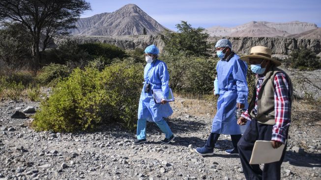 Petugas kesehatan berjalan di tepi Sungai Camana untuk menyuntik warga lanjut usia dengan dosis vaksin Pfizer-BioNTech melawan COVID-19 di Arequipa, Peru, pada (2/7/2021). [Diego Ramos / AFP]