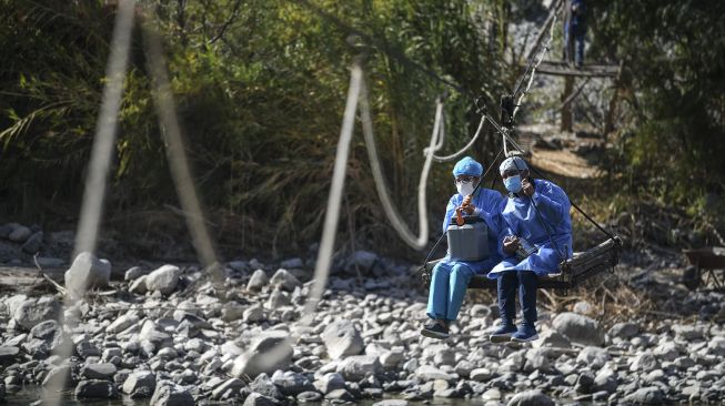 Petugas kesehatan menyeberangi Sungai Camana untuk menyuntik warga lanjut usia dengan dosis vaksin Pfizer-BioNTech melawan COVID-19 di Arequipa, Peru, pada (2/7/2021). [Diego Ramos / AFP]