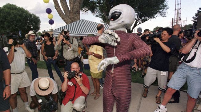 Seorang pria berpakaian alien dikelilingi oleh wartawan selama kompetisi kostum Festival UFO di pusat kota Roswell, New Mexico, pada (3/7/2021). [HECTOR MATA / AFP]