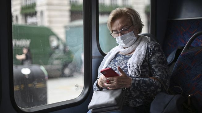 Seorang penumpang mengenakan masker memeriksa teleponnya saat bepergian dengan bus di sepanjang Oxford Street, Kota London, pada (5/7/2021). [DANIEL LEAL-OLIVAS / AFP]