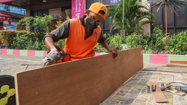 Petugas memotong kayu saat pembuatan peti mati di Kantor Kelurahan Kayu Putih, Jakarta Timur, Selasa (6/7/2021). [Suara.com/Alfian Winanto]