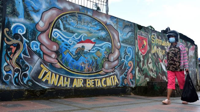 Warga mengenakan masker saat berjalan di dekat sebuah mural di Kota Ambon, Maluku, Rabu (7/7/2021).  ANTARA FOTO/FB Anggoro