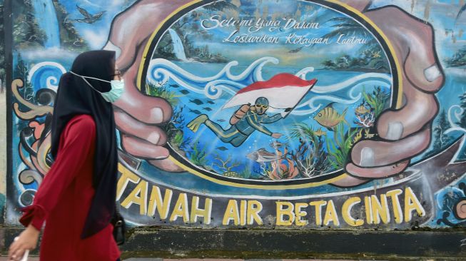 Warga mengenakan masker saat berjalan di dekat sebuah mural di Kota Ambon, Maluku, Rabu (7/7/2021).  ANTARA FOTO/FB Anggoro