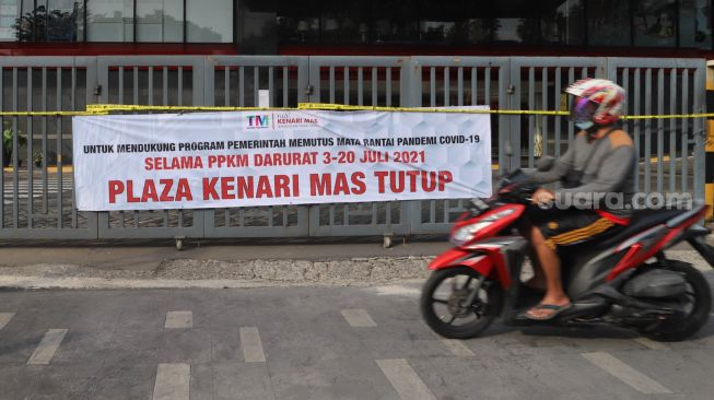 Warga melintas di depan spanduk berisi informasi penutupan Plaza Kenari Mas di kawasan Senen, Jakarta Pusat, Kamis (8/7/2021). [Suara.com/Alfian Winanto]