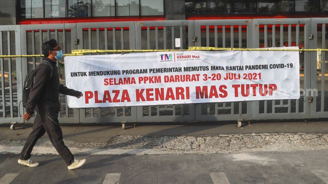 Warga melintas di depan spanduk berisi informasi penutupan Plaza Kenari Mas di kawasan Senen, Jakarta Pusat, Kamis (8/7/2021). [Suara.com/Alfian Winanto]