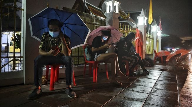 Warga menggunakan ponsel mereka saat mengantre semalaman untuk swab test COVID-19 gratis di Wat Phra Sri Mahathat Woramahawihan, Bangkok, pada (9/7/2021) dini hari. [Lillian SUWANRUMPHA / AFP]