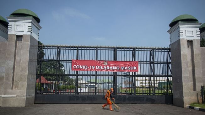 Pekerja menyapu dengan latar belakang gerbang dengan spanduk bertulis "COVID-19 Dilarang Masuk" di kompleks Parlemen, Jakarta, Jumat (9/7/2021). ANTARA FOTO/Aditya Pradana Putra.