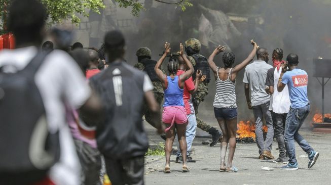 
Orang-orang membakar ban saat kerumunan mengelilingi kantor Polisi Petionville di mana orang-orang bersenjata yang dituduh terlibat dalam pembunuhan Presiden Jovenel Moïse di Port au Prince, Haiti, pada (8/7/2021). [Valerie Baeriswyl / AFP]