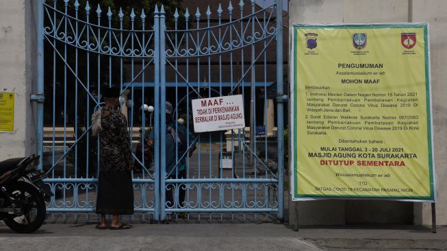 Warga melintas didepan pemberitahuan ditiadakan Shalat Jumat, di Masjid Agung Solo, Jawa Tengah, Jumat (9/7/2021). ANTARA FOTO/Maulana Surya