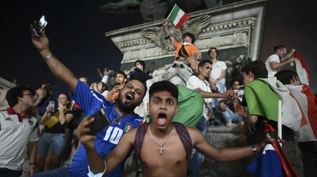 Pendukung tim sepak bola nasional Italia merayakan kemenangan setelah Italia mengalahkan Inggris pada final UEFA EURO 2020 di Piazza del Duomo, Milan pada (11/7/2021). [Marco BERTORELLO / AFP]