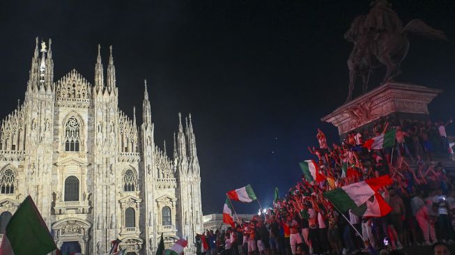 Pendukung tim sepak bola nasional Italia merayakan kemenangan setelah Italia mengalahkan Inggris pada final UEFA EURO 2020 di Piazza del Duomo, Milan pada (11/7/2021). [Marco BERTORELLO / AFP]