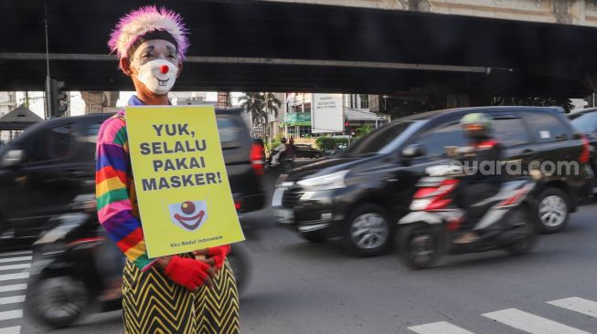 Angggota Komunitas Aku Badut Indonesia (ABI) membawa poster berisi ajakan untuk menggunakan masker di kawasan Cilandak, Jakarta Selatan, Senin (12/7/2021). [Suara.com/Alfian Winanto]