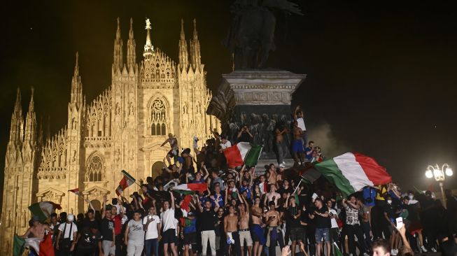 Pendukung tim sepak bola nasional Italia merayakan kemenangan setelah Italia mengalahkan Inggris pada final UEFA EURO 2020 di Piazza del Duomo, Milan pada (11/7/2021). [Marco BERTORELLO / AFP]