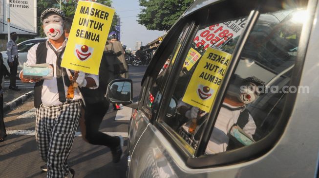 Angggota Komunitas Aku Badut Indonesia (ABI) membagi-bagikan masker kepada pengendara motor saat melakukan aksi kampanye untuk menggunakan masker di kawasan Cilandak, Jakarta Selatan, Senin (12/7/2021). [Suara.com/Alfian Winanto]