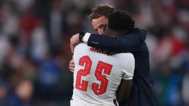 Pelatih Inggris Gareth Southgate berbicara kepada gelandang Inggris Bukayo Saka setelah kekalahan mereka dalam adu penalti melawan Italia di  final UEFA EURO 2020 di Stadion Wembley, London pada 11 Juli 2021. Laurence Griffiths / POOL / AFP