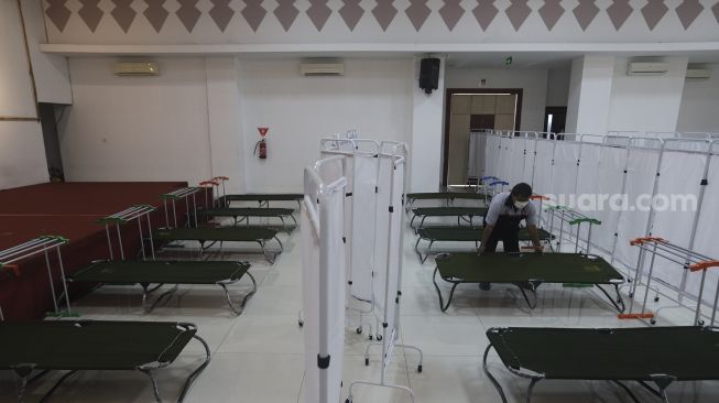 Petugas menyiapkan velbed  bagi warga yang akan menjalani isolasi mandiri di GOR Kecamatan Matraman, Jakarta, Selasa (13/7/2021). [Suara.com/Angga Budhiyanto]