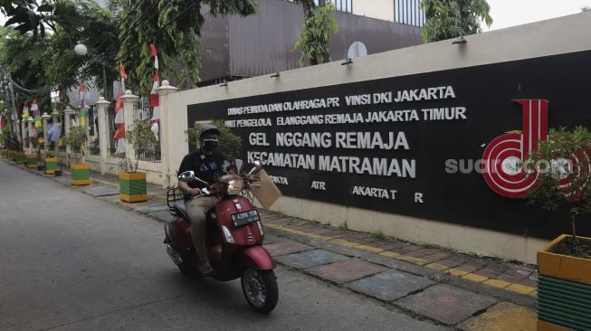 Pengendara sepeda motor melintas di depan GOR Kecamatan Matraman yang dijadikan tempat isolasi mandiri, di Jakarta, Selasa (13/7/2021). [Suara.com/Angga Budhiyanto]