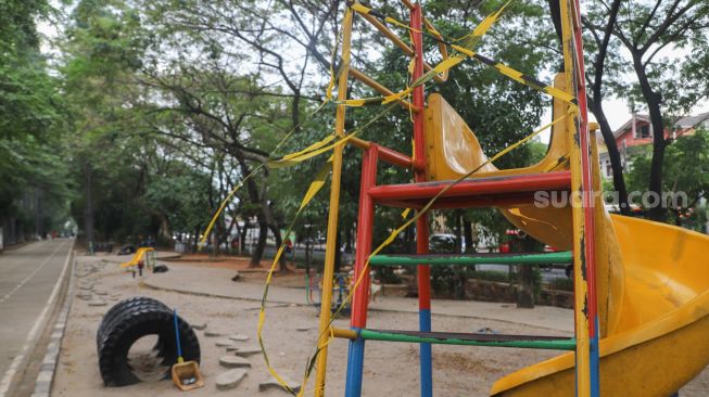 Area bermain anak yang diberi garis pembatas agar tidak digunakan di kawasan Banjir Kanal Timur (BKT), Jakarta Timur, Rabu (14/7/2021). [Suara.com/Alfian Winanto]