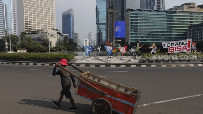 Seorang warga berjalan di dekat maskot dan slogan Pekan Olahraga Nasional (PON) XX Papua di Bundaran Hotel Indonesia, Jakarta, Jumat (16/7/2021). [Suara.com/Angga Budhiyanto]