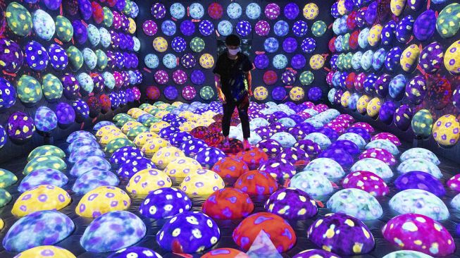 Seorang petugas berjalan melalu instalasi digital interaktif bernama "Rapidly Rotating Bouncing Sphere Caterpillar House" selama pratinjau media "teamLab Forest" di gedung hiburan BOSS E・ZO FUKUOKA, Fukuoka, Jepang, pada (16/7/2021). [Yuki IWAMURA / AFP]