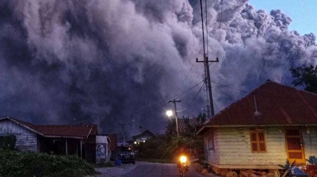 Sejumlah pengendara melintas di Jalan Karo-Langkat dengan latar belakang Gunung Sinabung yang menyemburkan material vulkanik di Desa Kutarayat, Naman Teran, Karo, Sumatera Utara, Senin (19/7/2021). ANTARA FOTO/Sastrwawan Ginting
