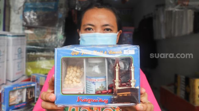 Pedagang menunjukkan paket oleh-oleh khas haji yang berisi air zam-zam, kurma dan juga kacang arab di sekitar kawasan Asrama Haji Pondok Gede, Jakarta Timur, Kamis (22/7/2021). [Suara.com/Alfian Winanto] 