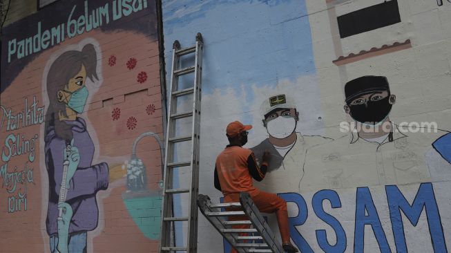 Pekerja Penanganan Sarana dan Prasarana Umum (PPSU) menyelesaikan mural melawan COVID-19 di tembok di kawasan Cikokol, Cawang, Jakarta, Jumat (23/7/2021). [Suara.com/Angga Budhiyanto]