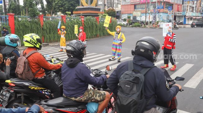 Angggota Komunitas Aku Badut Indonesia (ABI) melakukan aksi kampanye untuk mengajak masyarakat melakukan vaksinasi dan mematuhi protokol kesehatan di Kawasan Juanda, Depok, Jawa Barat, Jumat (23/7/2021). [Suara.com/Alfian Winanto]