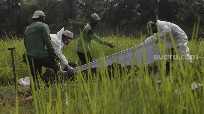 Petugas memakamkan jenazah yang meninggal dunia karena COVID-19 di TPU Tegal Alur, Jakarta, Jumat (23/7/2021). [Suara.com/Angga Budhiyanto]