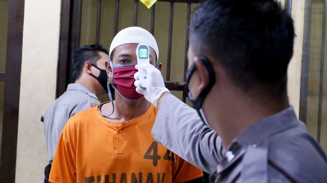 Petugas kepolisian memeriksa suhu badan tahanan yang akan mengikuti vaksinasi COVID-19 di Mapolres Blitar, Jawa Timur, Jumat (23/7/2021). ANTARA FOTO/Irfan Anshori
