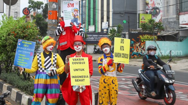 Angggota Komunitas Aku Badut Indonesia (ABI) melakukan aksi kampanye untuk mengajak masyarakat melakukan vaksinasi dan mematuhi protokol kesehatan di Kawasan Juanda, Depok, Jawa Barat, Jumat (23/7/2021). [Suara.com/Alfian Winanto]