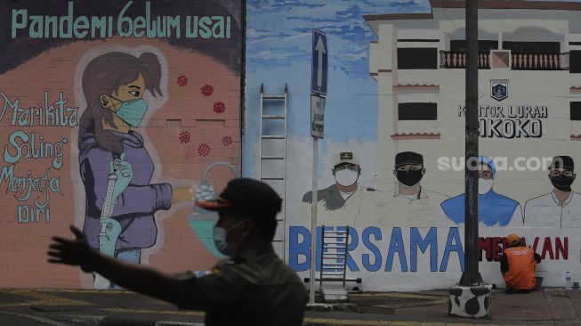 Pekerja Penanganan Sarana dan Prasarana Umum (PPSU) menyelesaikan mural melawan COVID-19 di tembok di kawasan Cikokol, Cawang, Jakarta, Jumat (23/7/2021). [Suara.com/Angga Budhiyanto]