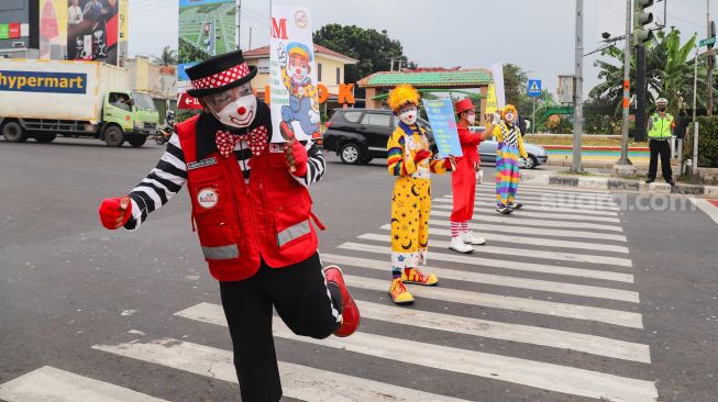 Angggota Komunitas Aku Badut Indonesia (ABI) melakukan aksi kampanye untuk mengajak masyarakat melakukan vaksinasi dan mematuhi protokol kesehatan di Kawasan Juanda, Depok, Jawa Barat, Jumat (23/7/2021). [Suara.com/Alfian Winanto]