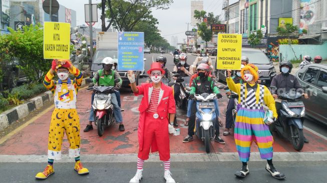 Angggota Komunitas Aku Badut Indonesia (ABI) melakukan aksi kampanye untuk mengajak masyarakat melakukan vaksinasi dan mematuhi protokol kesehatan di Kawasan Juanda, Depok, Jawa Barat, Jumat (23/7/2021). [Suara.com/Alfian Winanto]