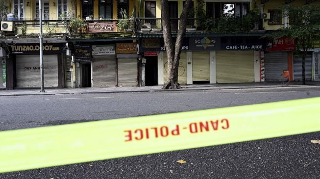 Toko-toko dan restoran-restoran yang tutup di sepanjang jalan yang sepi di Hanoi, Vietnam, Sabtu (24/7/2021). [Manan VATSYAYANA / AFP]