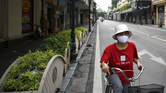 Un habitant portant un masque fait du vélo dans une rue presque vide à Hanoï, au Vietnam, samedi (24/07/2021). [Manan VATSYAYANA / AFP]