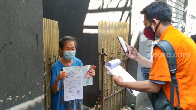 Petugas Pos Indonesia mendokumentasikan warga yang sudah mendapatkan Bantuan Sosial Tunai (BST) di kawasan Glodok, Jakarta Barat, Minggu (25/7/2021). [Suara.com/Alfian Winanto]