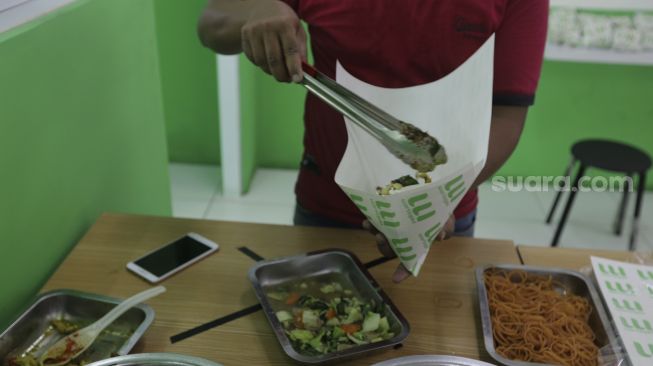 Pekerja membungkus makanan di Wartegan, Ampera, Jakarta, Senin (26/7/2021). [Suara.com/Angga Budhiyanto]