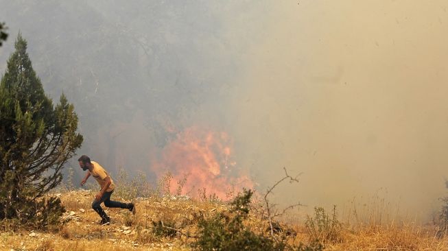 Seorang pria berlari mencari perlindungan saat petugas pemadam kebakaran memadamkan api di hutan daerah Qubayyat di wilayah terpencil Akkar, Lebanon, pada (29/7/2021). [JOSEPH EID / AFP]