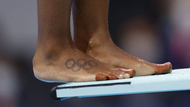 Tato cincin Olimpiade terlihat di kaki Jennifer Abel dari Kanada saat dia bersiap untuk berkompetisi dalam laga final loncatan 3 meter putri selama Olimpiade Tokyo 2020 di Tokyo Aquatics Center, Tokyo pada (25/7/2021). [Odd ANDERSEN / AFP]