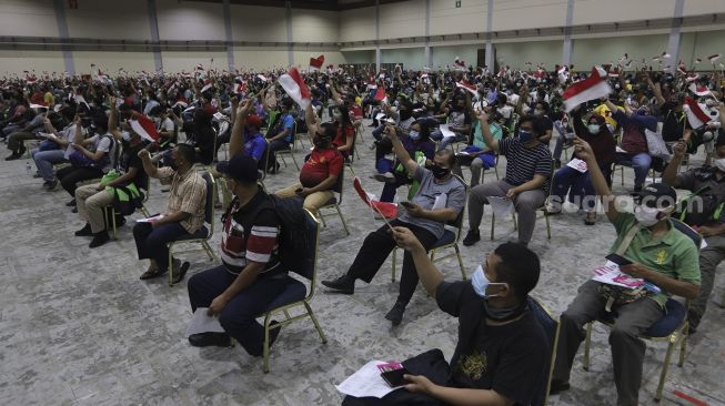 Sejumlah warga mengibarkan bendera Merah Putih saat mengantre untuk mendapatkan vaksinasi COVID-19 di Jakarta Convention Center (JCC), Senayan, Jakarta, Sabtu (31/7/2021). [Suara.com/Angga Budhiyanto]